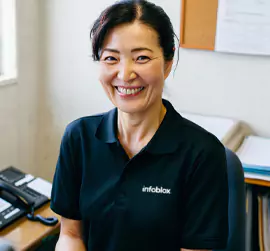 Smiling woman in an Infoblox polo shirt at her desk.