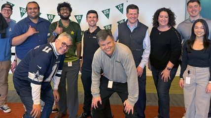 Group of coworkers smiling and posing together at a themed event with green flag decorations.